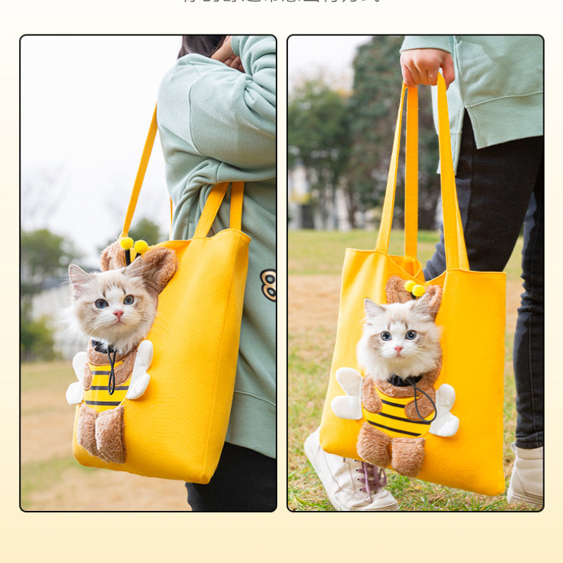 Cat in a bee costume inside a yellow bag held by a person outdoors.